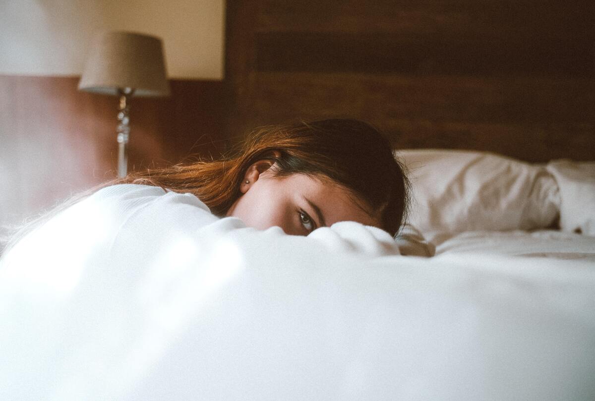 Mulher de cabeça baixa apoiada na cama.