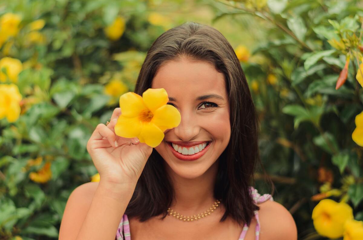 Mulher sorrindo segurando uma flor.