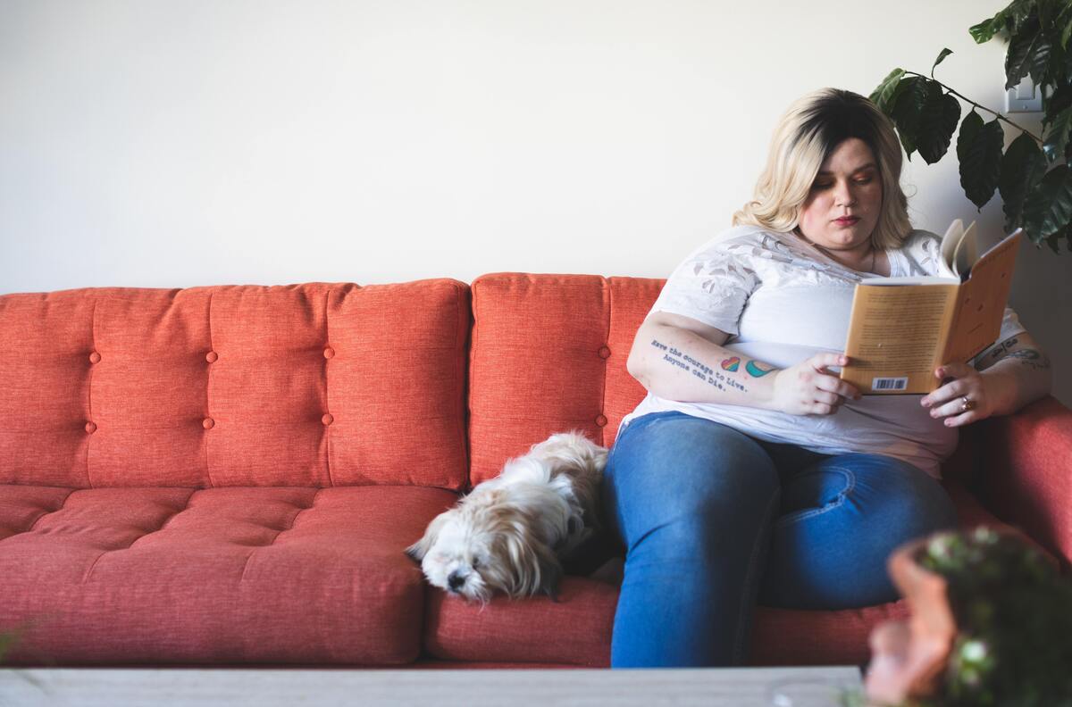 Mulher sentada no sofá, lendo um livro.