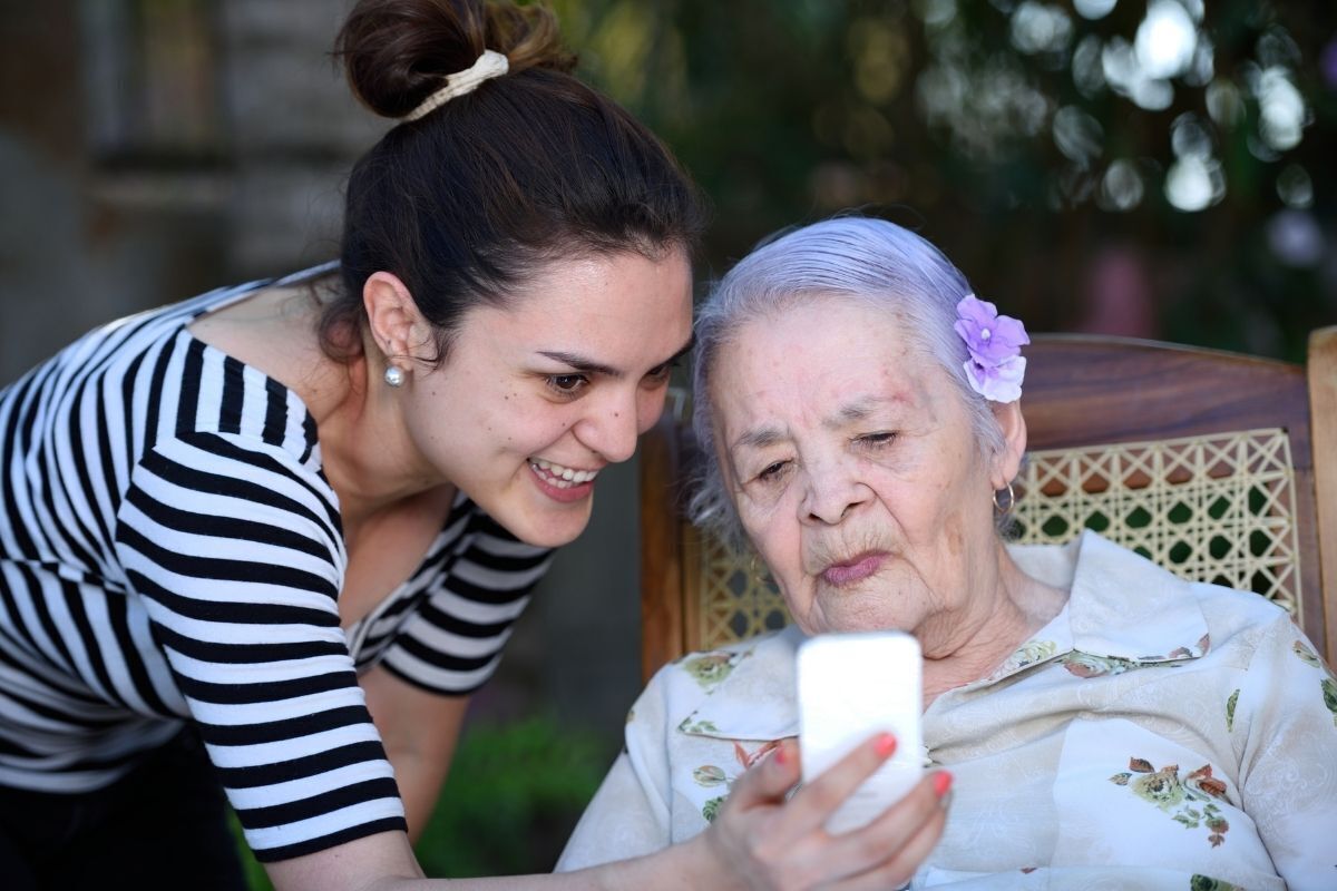 Tia e avó sentada na cadeira, olhando para o celular