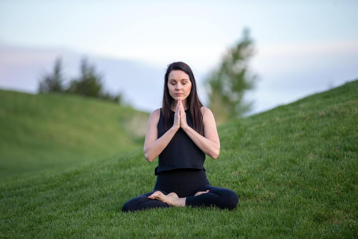 Mulher meditando em um campo gramado.