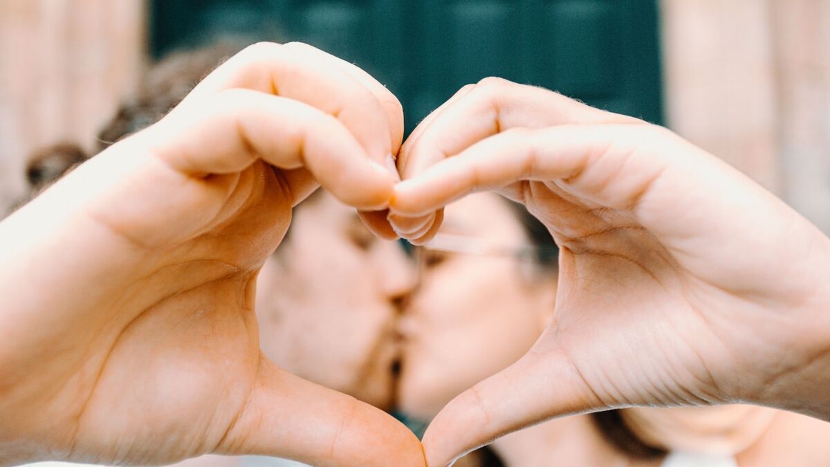 Casal se beijando e fazendo coração com as mãos.