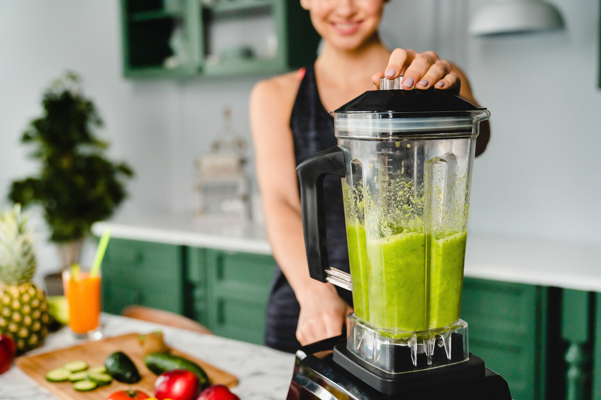 Mulher fazendo suco verde no liquidificador.