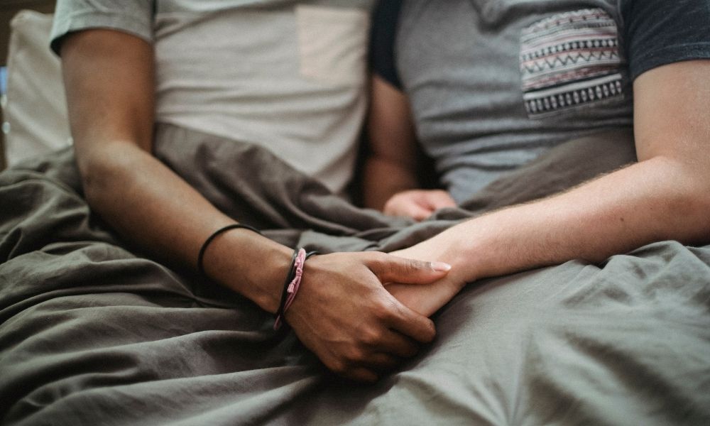 Casal de mãos dadas na cama.