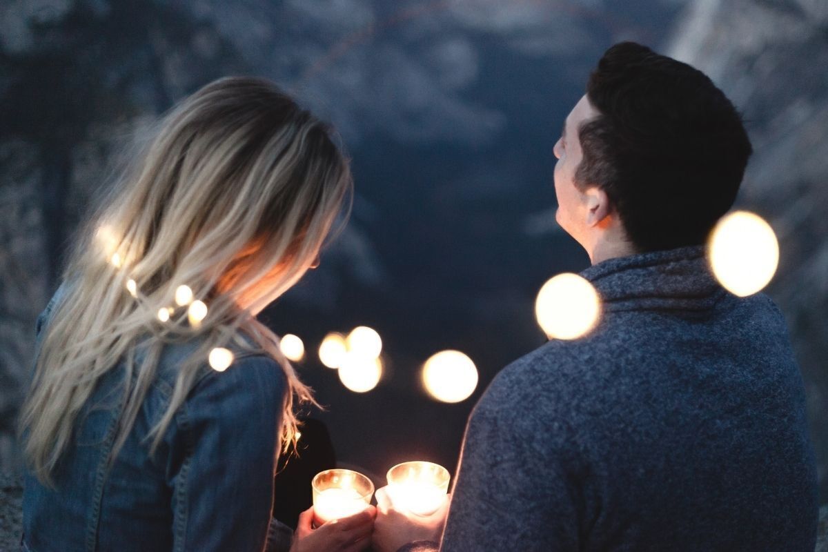 Casal de costas segurando uma vela envoltos de muito brilho e luz