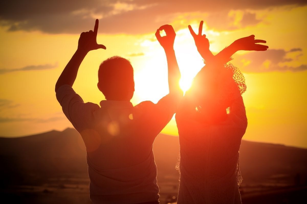 Casal comemorando o pôr do Sol, formando a palavra Love com as mãos