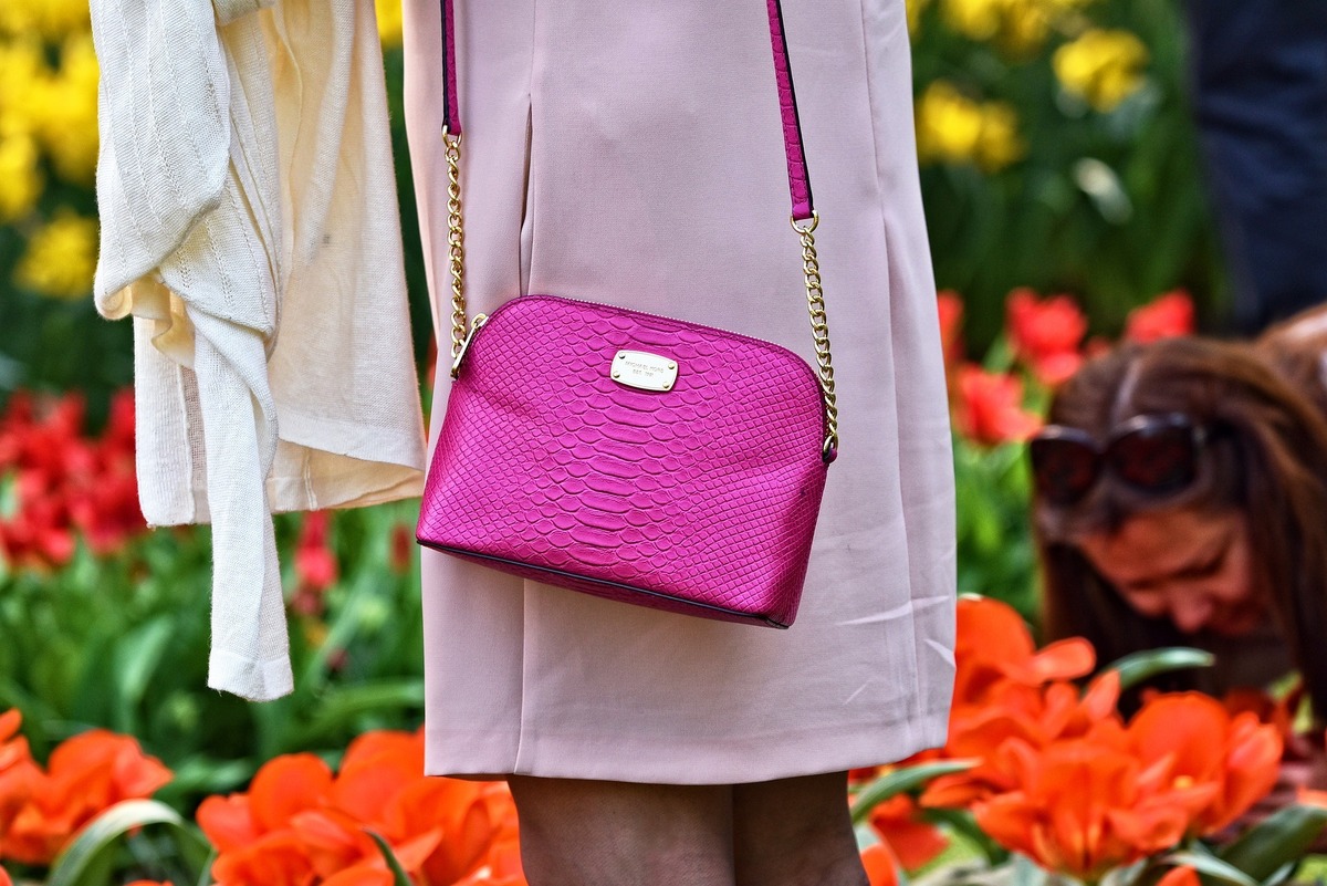 Mulher com bolsa pequena e rosa pendurada nas costas.