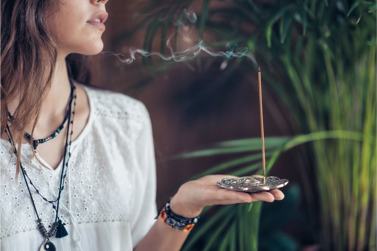 Mulher meditando com o incenso de alecrim em uma das suas mãos