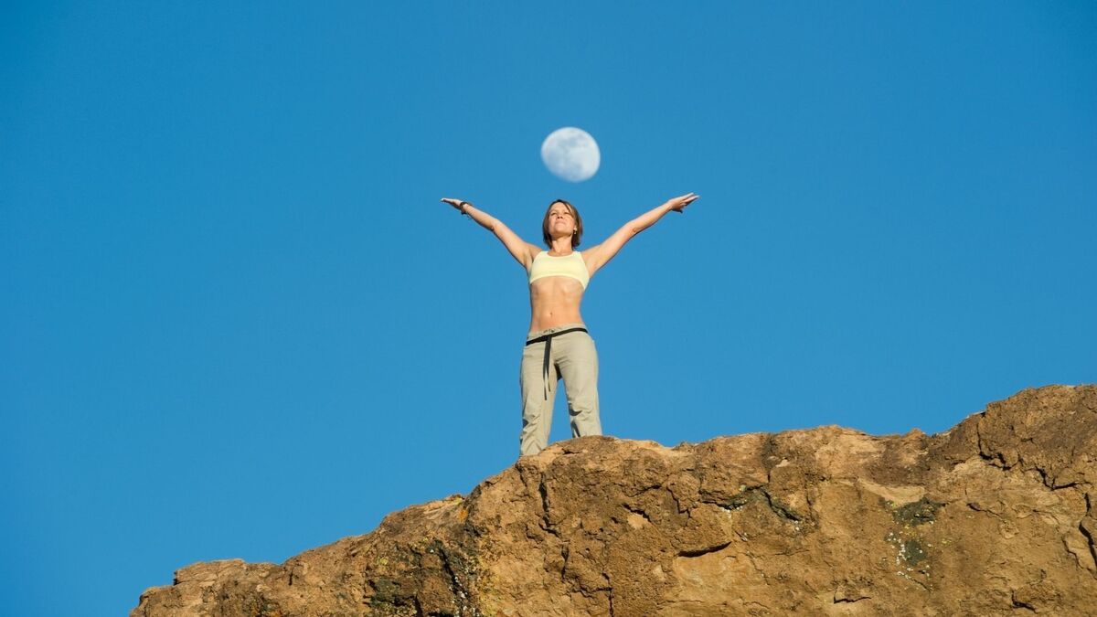 Mulher em cima de um morro e a lua cheia.