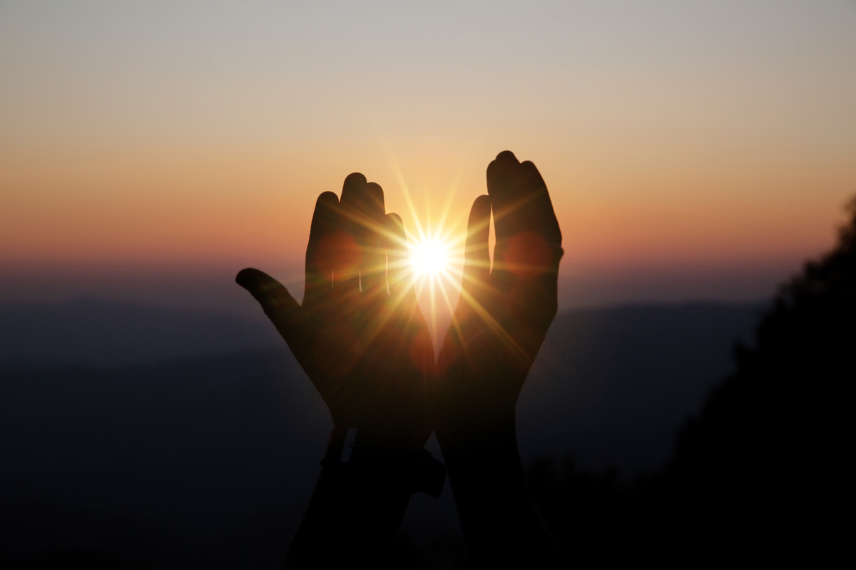 Mãos englobando o Sol em sinal de esperança.