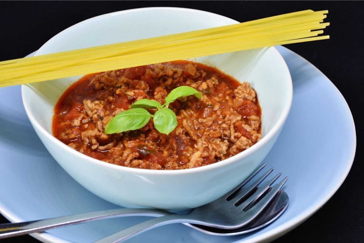 Carne moída em um prato branco e macarrão ainda crú