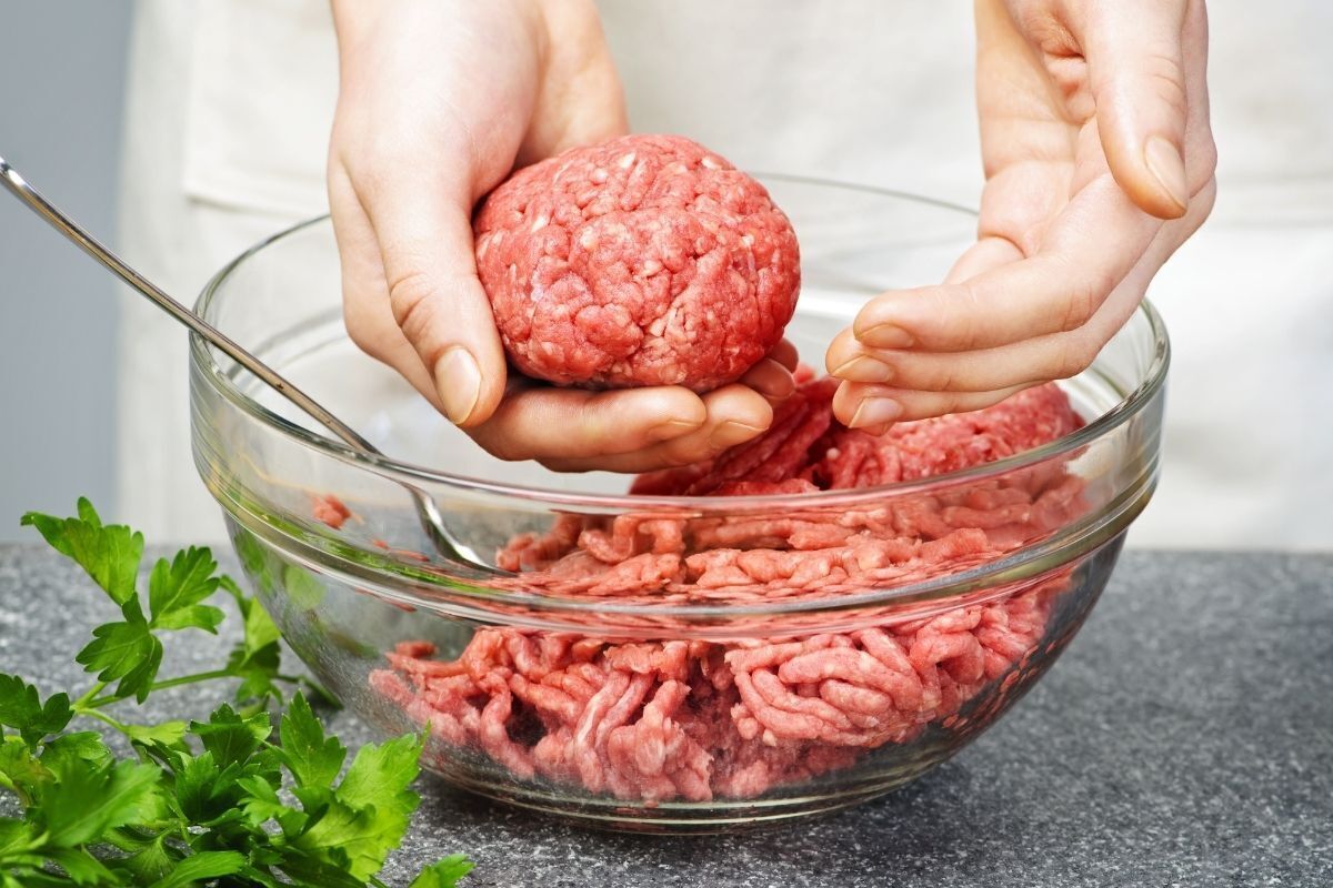 Mãos de uma pessoa formando bolinhos com a carne moída