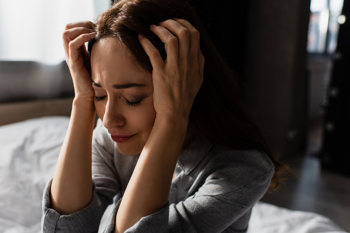 Mulher com expressão agonizada enquanto tem as mãos na cabeça, simbolizando o ato de tentar falar, mas não conseguir.