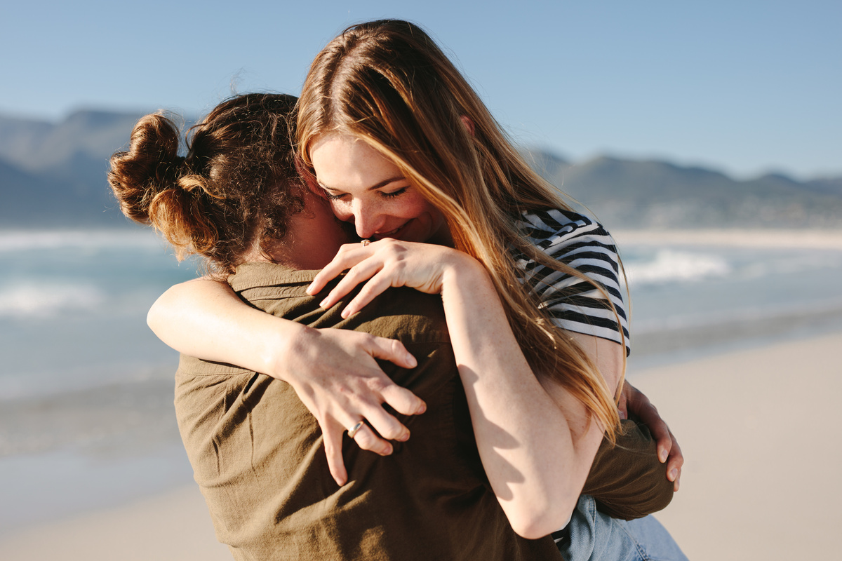 Casal de homem e mulher se abraçando na beira da praia, simbolizando a entrega aos sentimentos das pessoas com descendente em Sagitário.