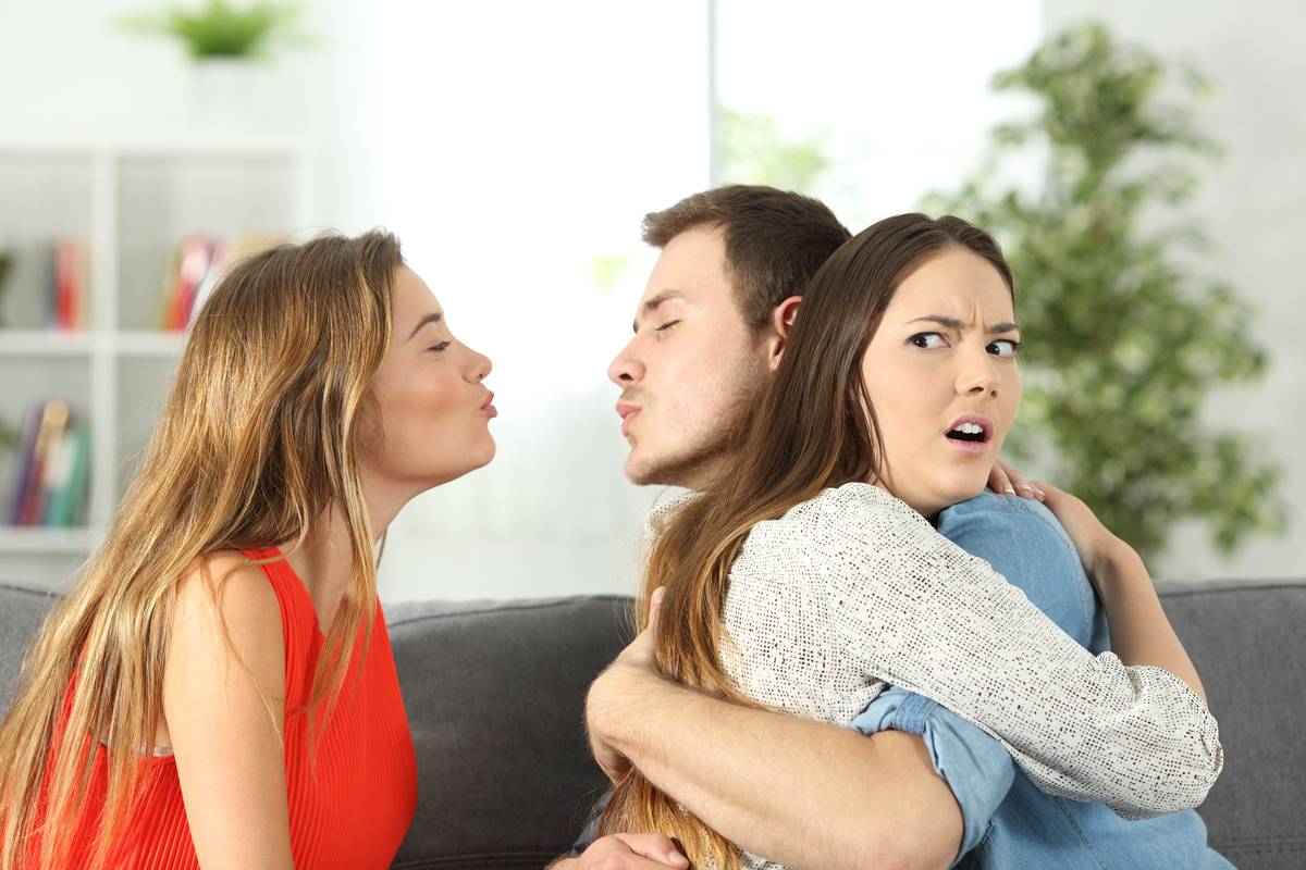 Namorada abraçando namorado enquanto ele flerta com outra mulher