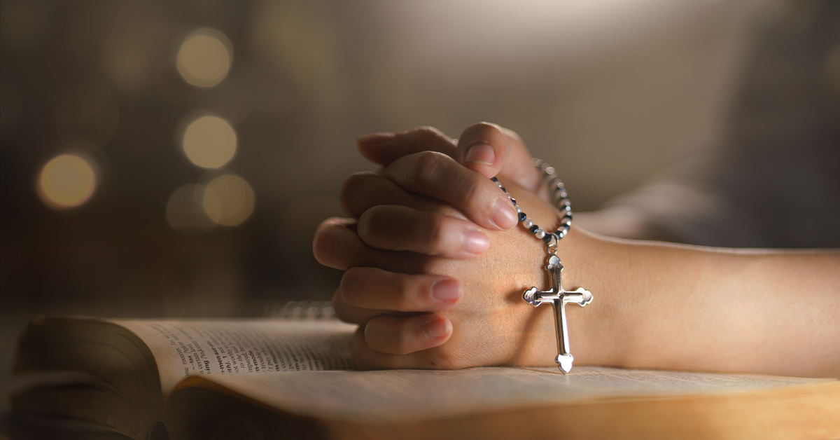 Mão com crucifixo em cima da mesa.