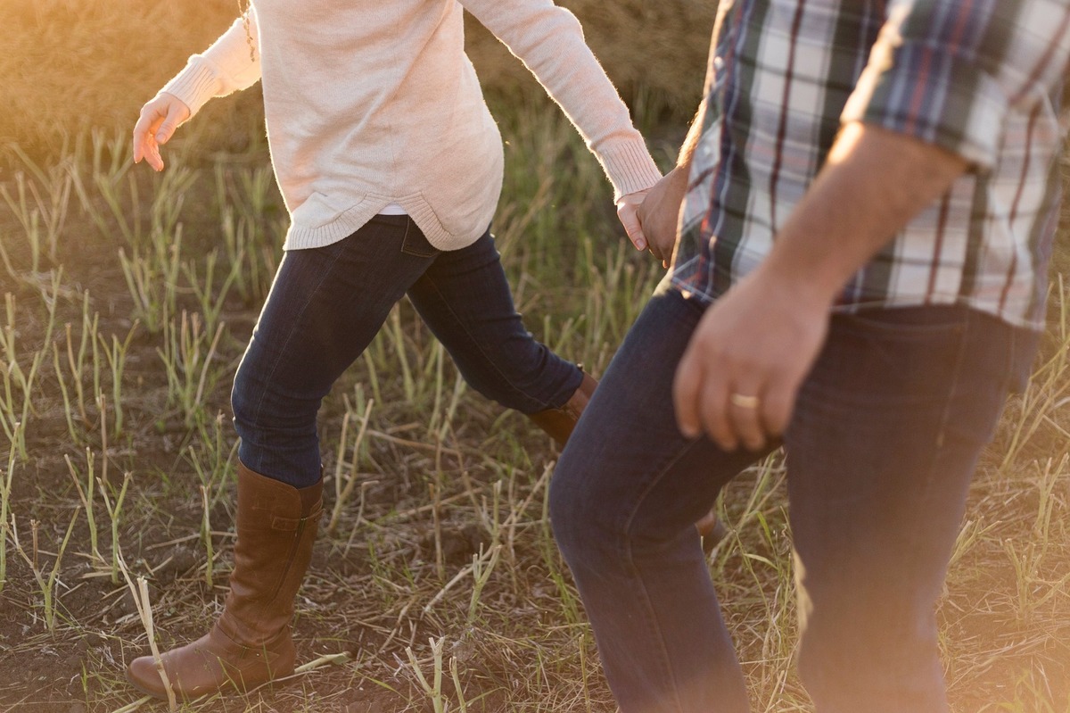 Casal de homem e mulher caminhando pelo campo enquanto estão de mãos dadas.