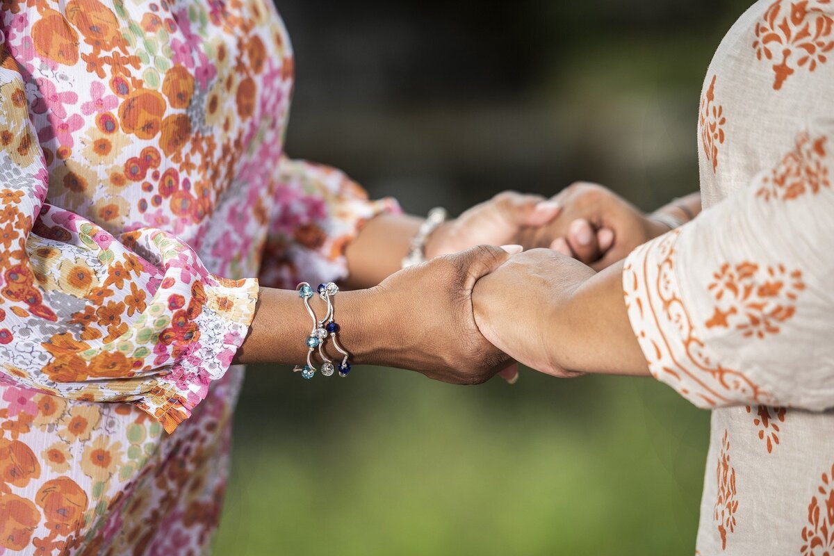 Duas mulheres com as duas mãos dadas uma para a outra.