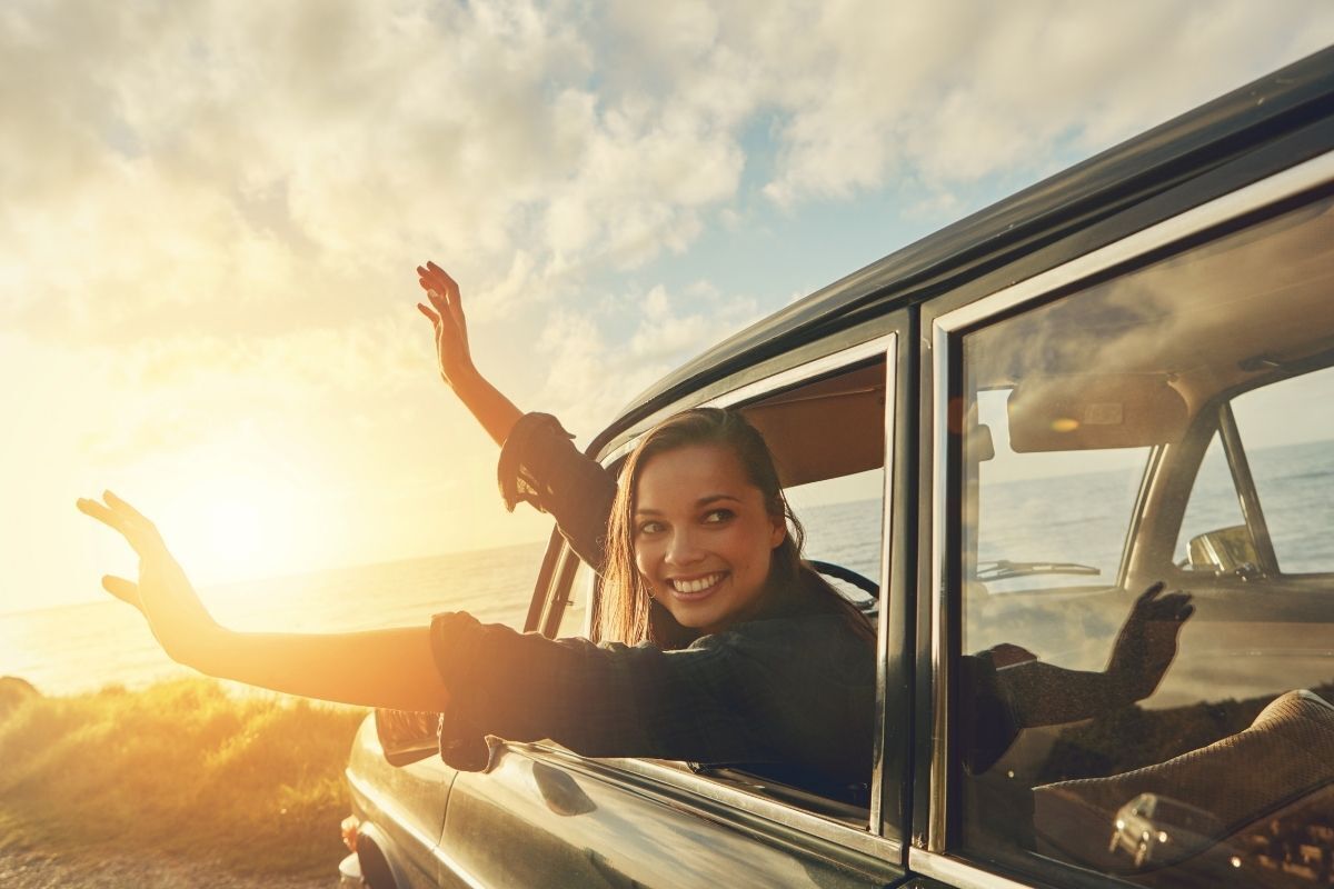 Mulher sorrindo com as mãos para fora da janela do carro, sentindo o vento.