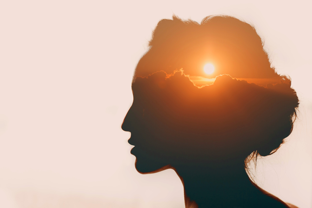 Montagem com contorno de rosto feminino e céu com sol poente dentro do rosto