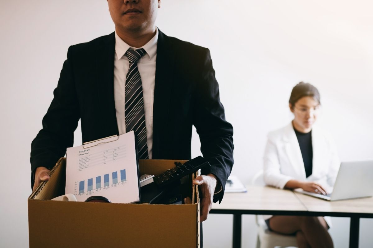 Homem sendo demitido do emprego, carregando uma caixa com seus pertences