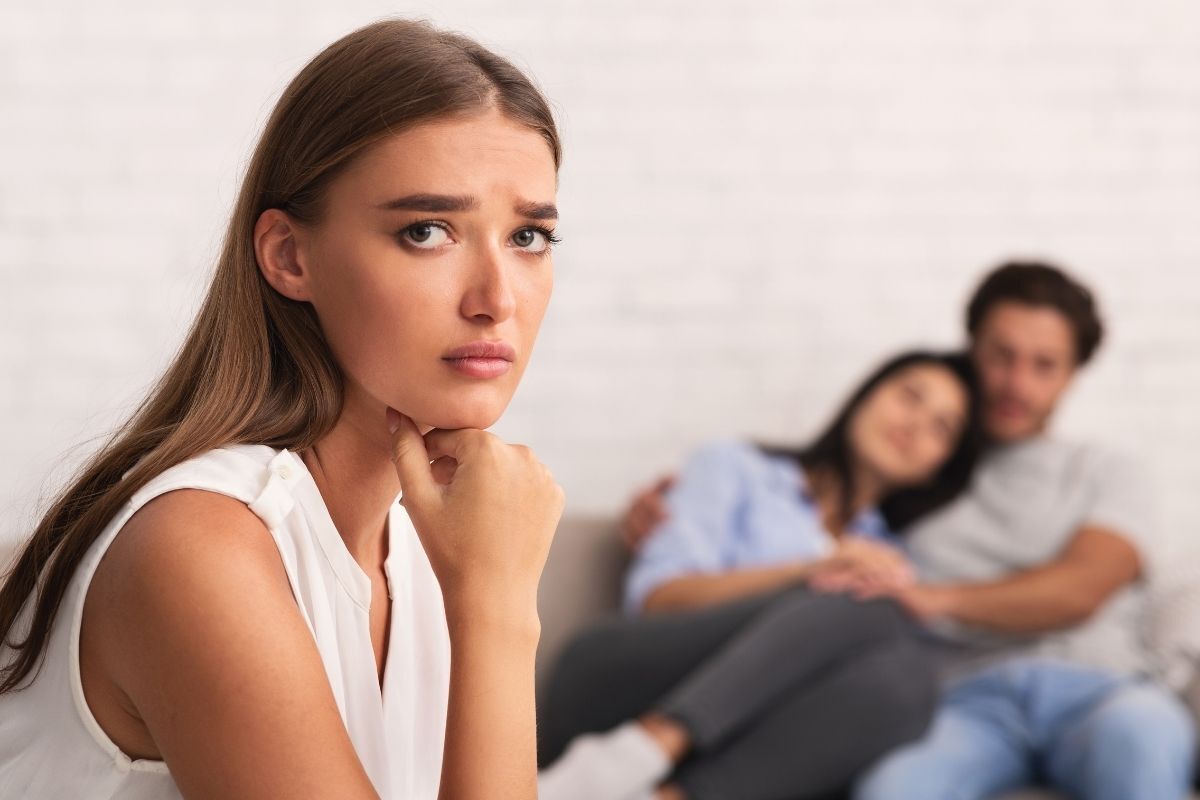 Mulher pensativa e angustiada, casal ao fundo desfocado