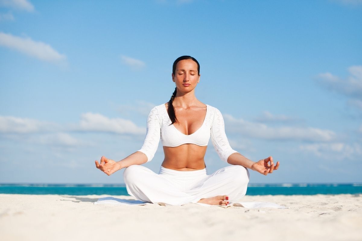 Mulher meditando na areia da praia