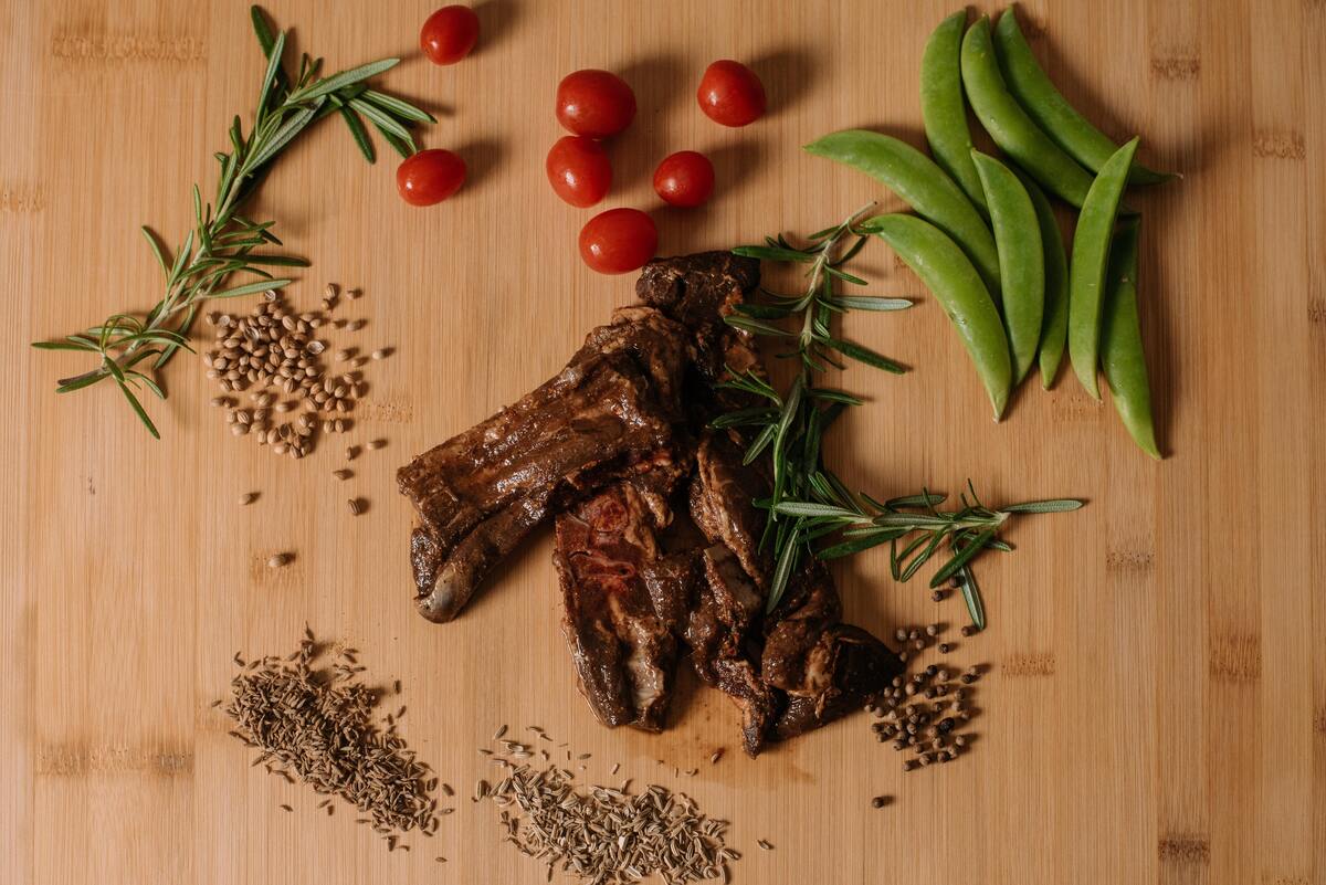 Pedaços fritos de carne com tomates, vagem e diversos temperos em volta. 