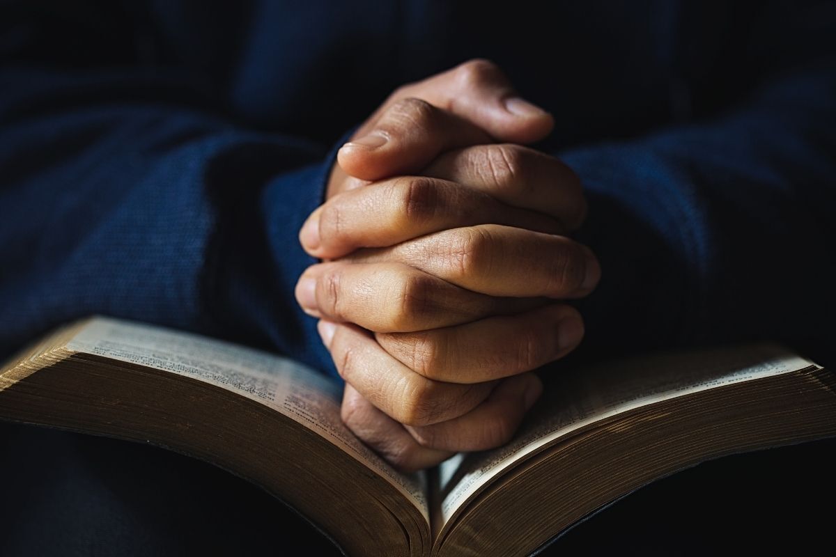 Mãos de uma pessoa rezando sob a bíblia