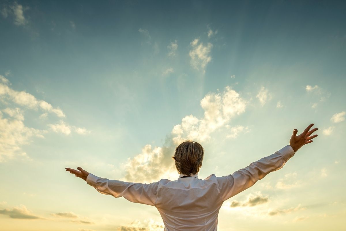 Homem com os braços abertos para o céu em forma de agradecimento