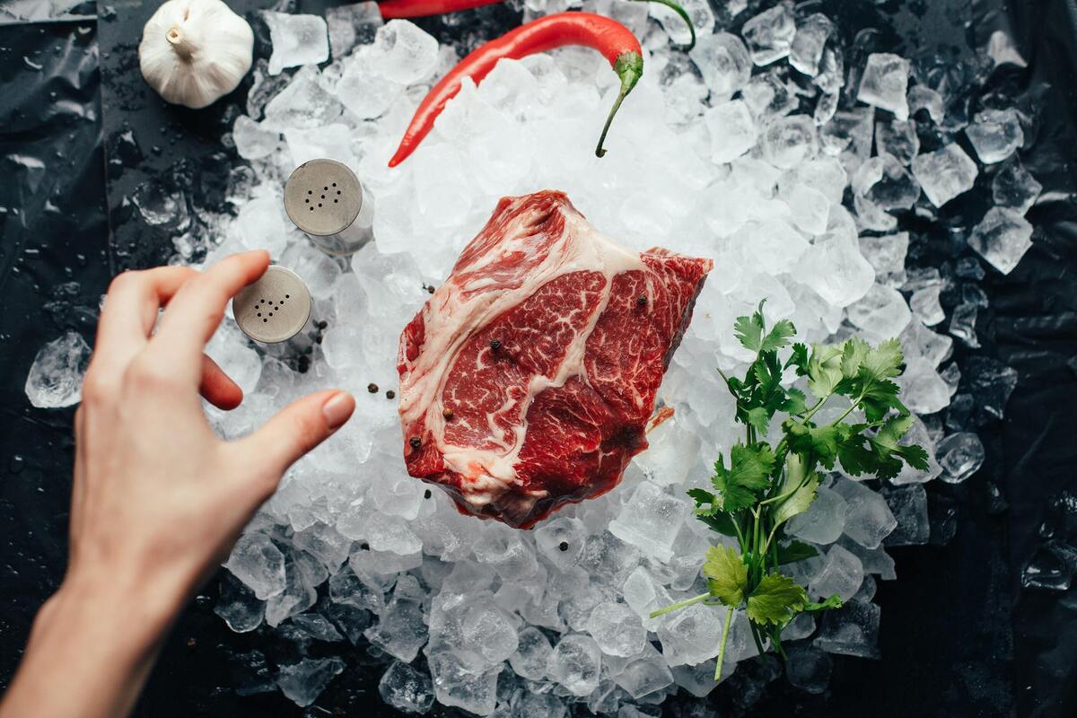 Carne em cima de gelo com alguns temperos ao lado. 