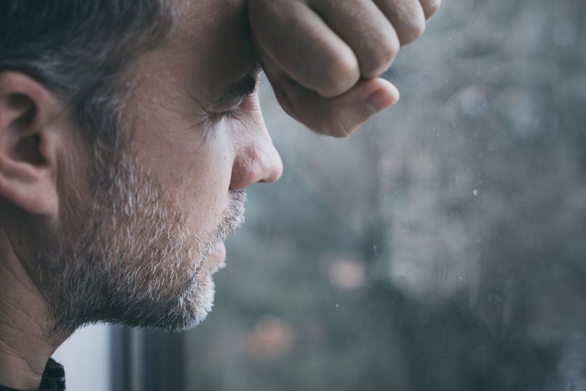 Homem com a cabeça encostada nas mãos sob o vidro