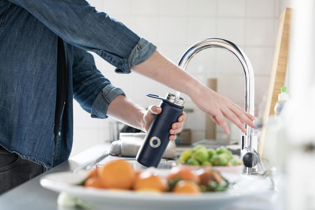 Pessoa enchendo garrafa na torneira da cozinha