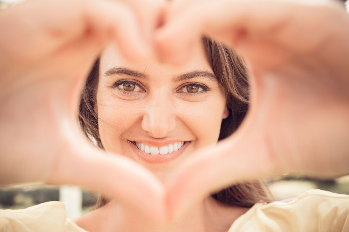 Mulher sorrindo com as mãos em formato de coração