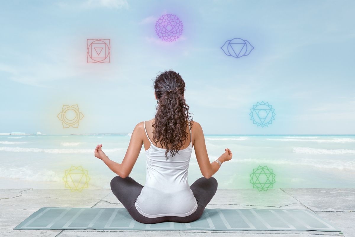 Mulher meditando em frente ao mar - ilustração dos chakras flutuando