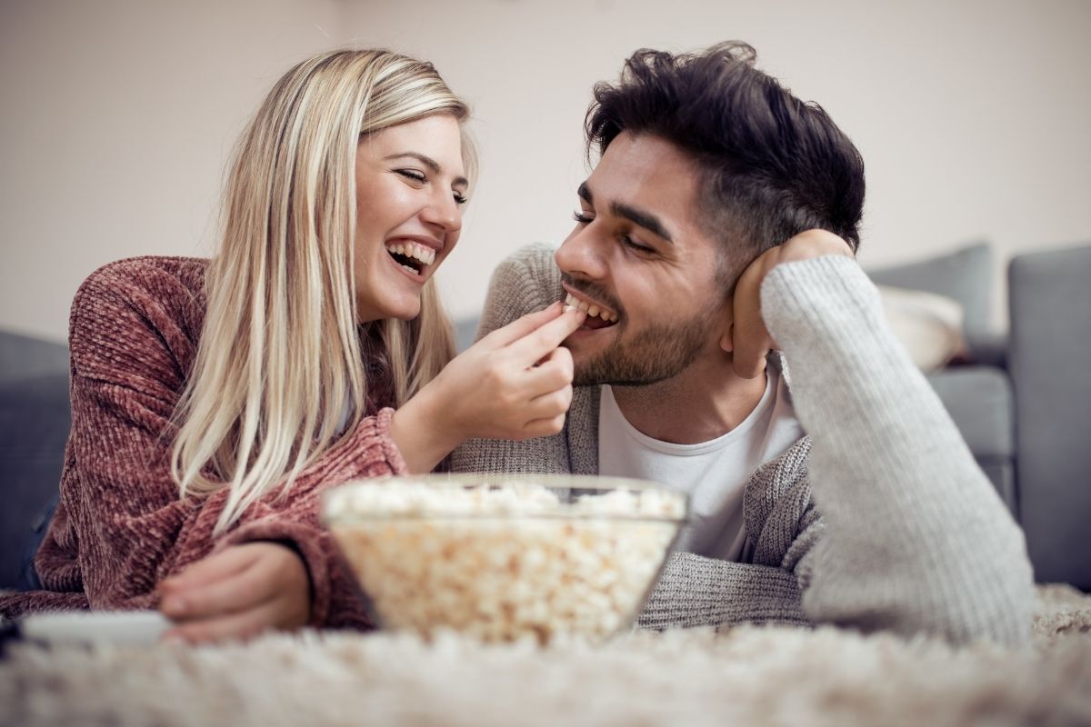 Casal deitado no chão da sala comendo pipoca