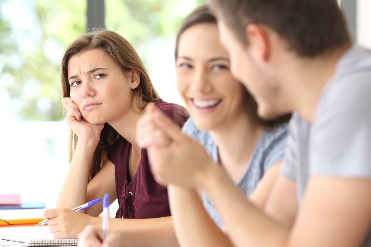 Mulher chateada com a mão no queixo ao ver amigos conversando