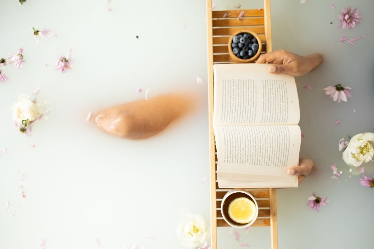 Mulher tomando banho de leite e lendo um livro na banheira