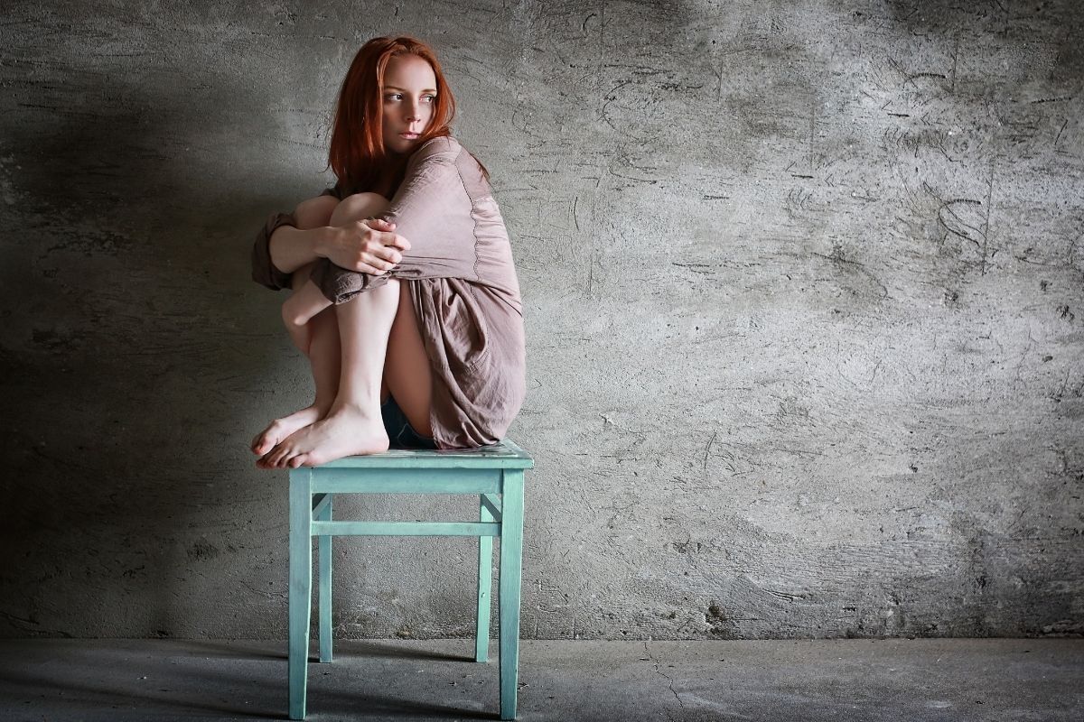 Mulher com expressão de medo, sentada em um banco de madeira