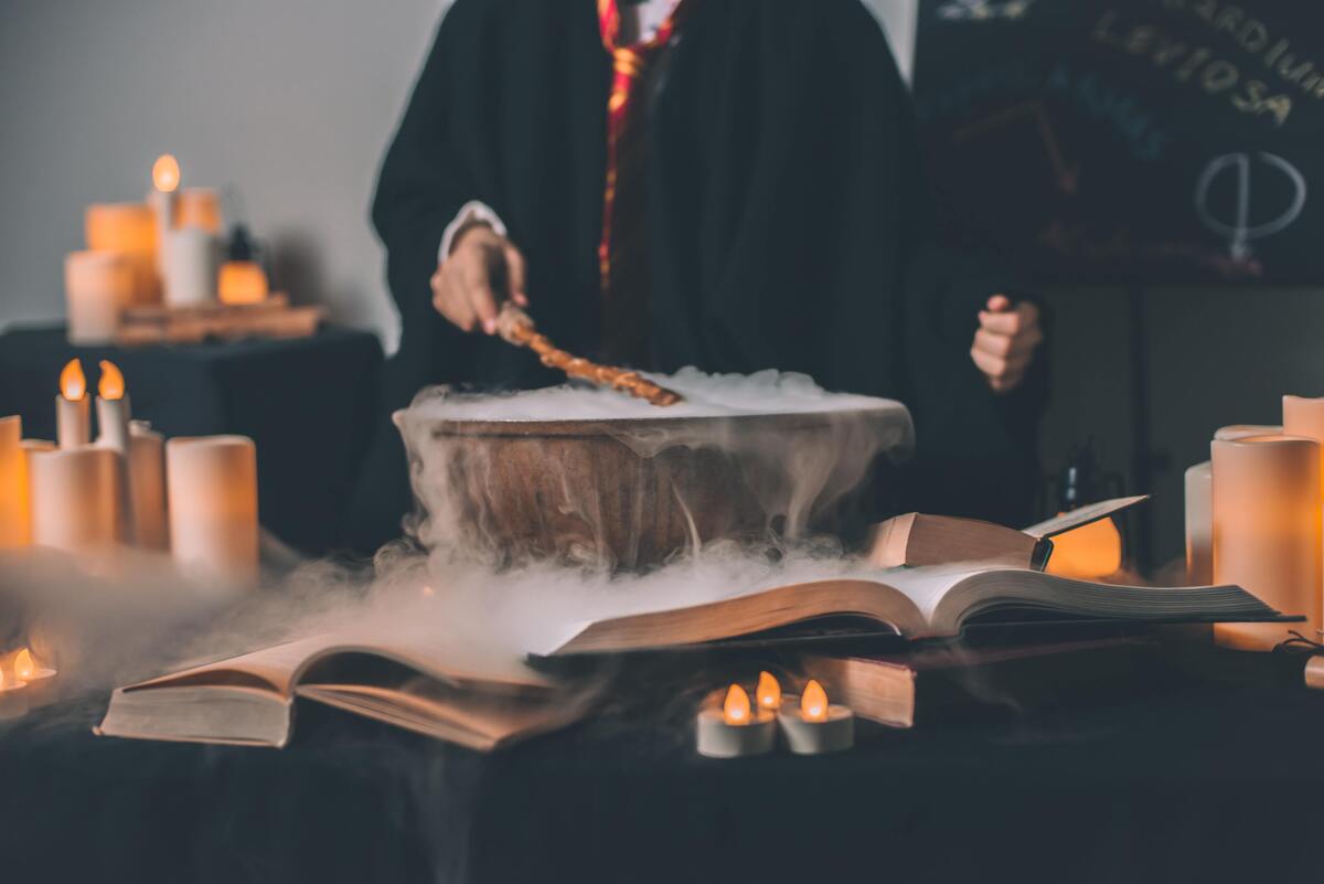 Pessoa fazendo feitiço em caldeirão com fumaça e com livros ao redor