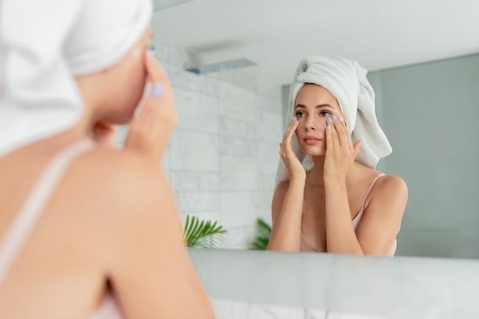 Mulher se olhando no espelho enquanto passa creme no rosto