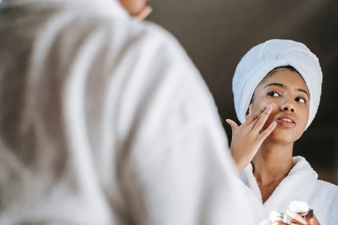 Reflexo de mulher passando creme na região dos olhos