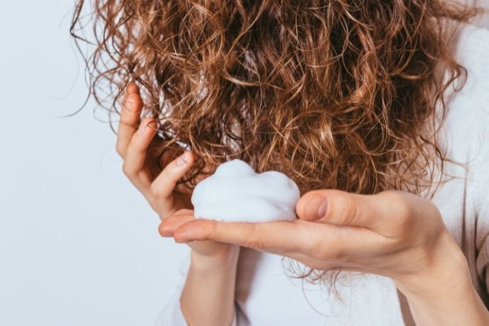 Mulher aplicando mousse em cabelo cacheado