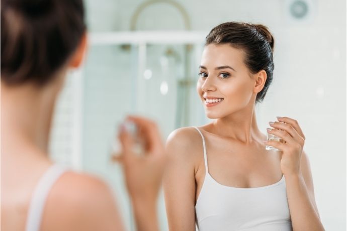 Mulher se olhando no espelho e colocando perfume