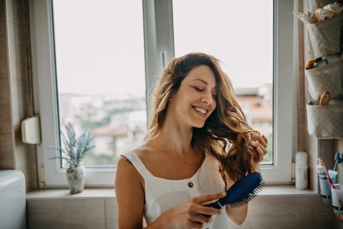 Mulher sorrindo enquanto penteia seu cabelo com escova