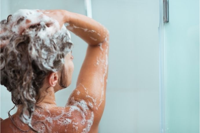 Mulher no banho lavando o cabelo com shampoo