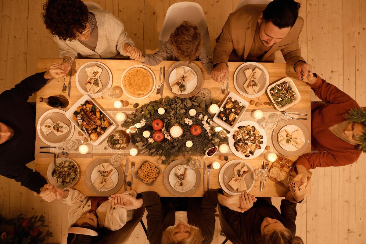 Família de mãos dadas ao redor de uma mesa farta