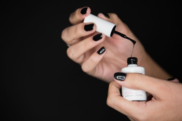 Mulher com unhas pretas segurando pote aberto de esmalte de unha preto