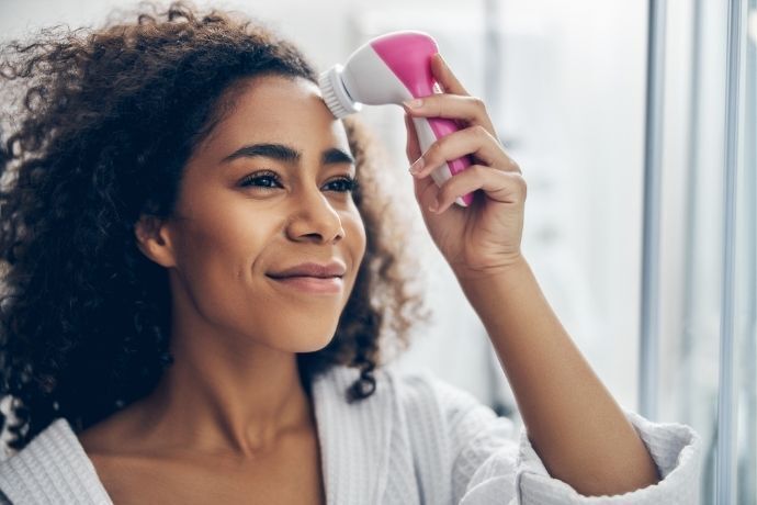 Mulher limpando o rosto com esponja elétrica