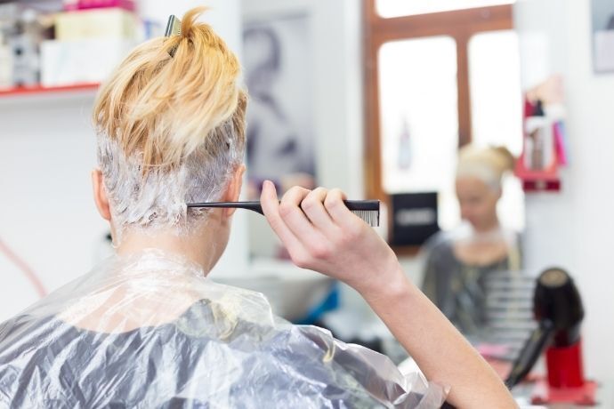 Mulher se olhando no espelho e pintando o cabelo de loiro claro